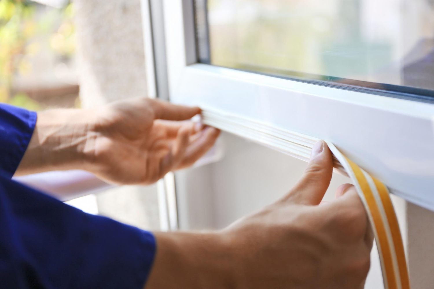 Hands fitting a sealing strip around a window frame to reduce air gaps